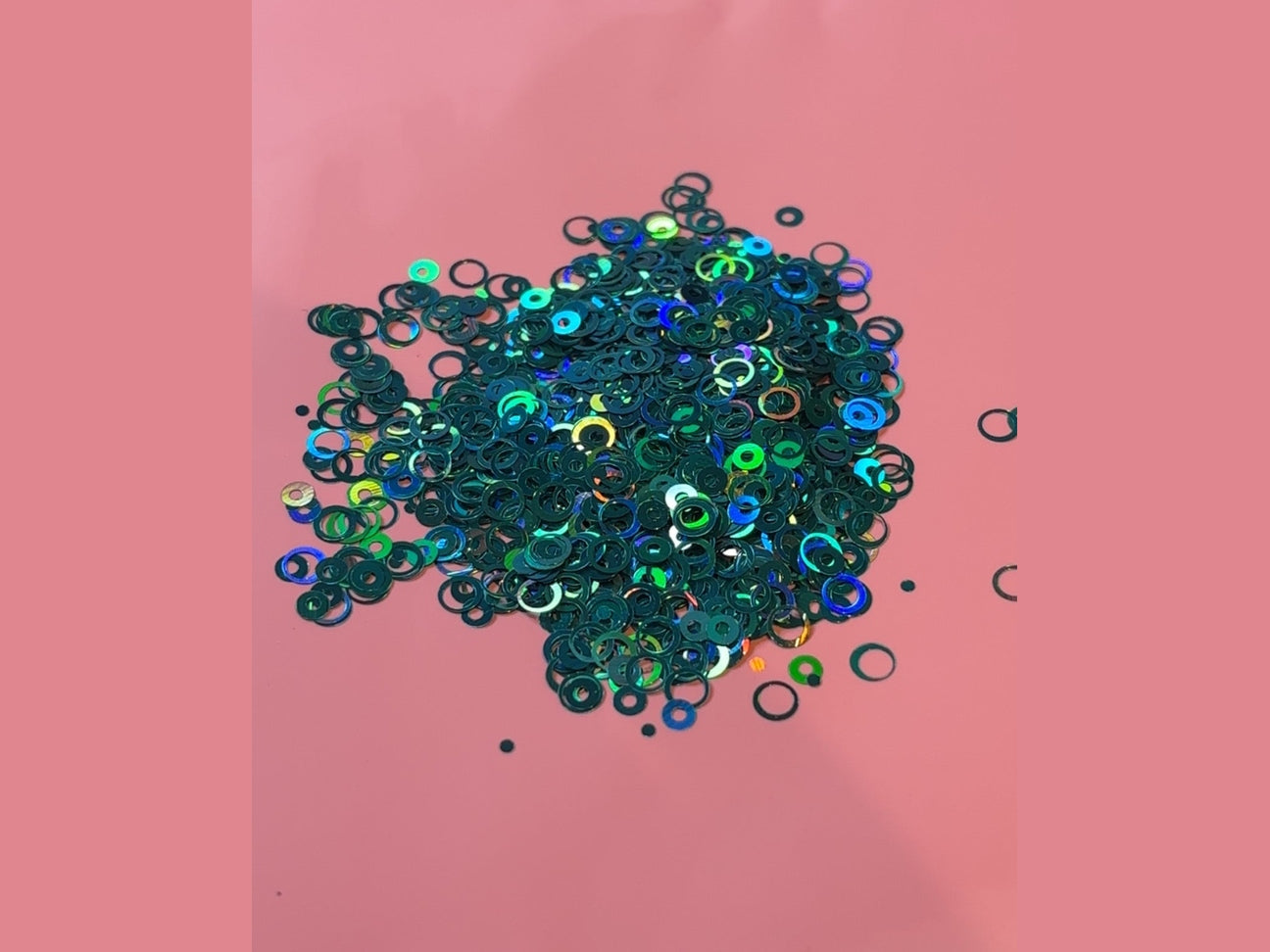Dark green iridescent glitter bubble rings with blue and gold highlights on pink background