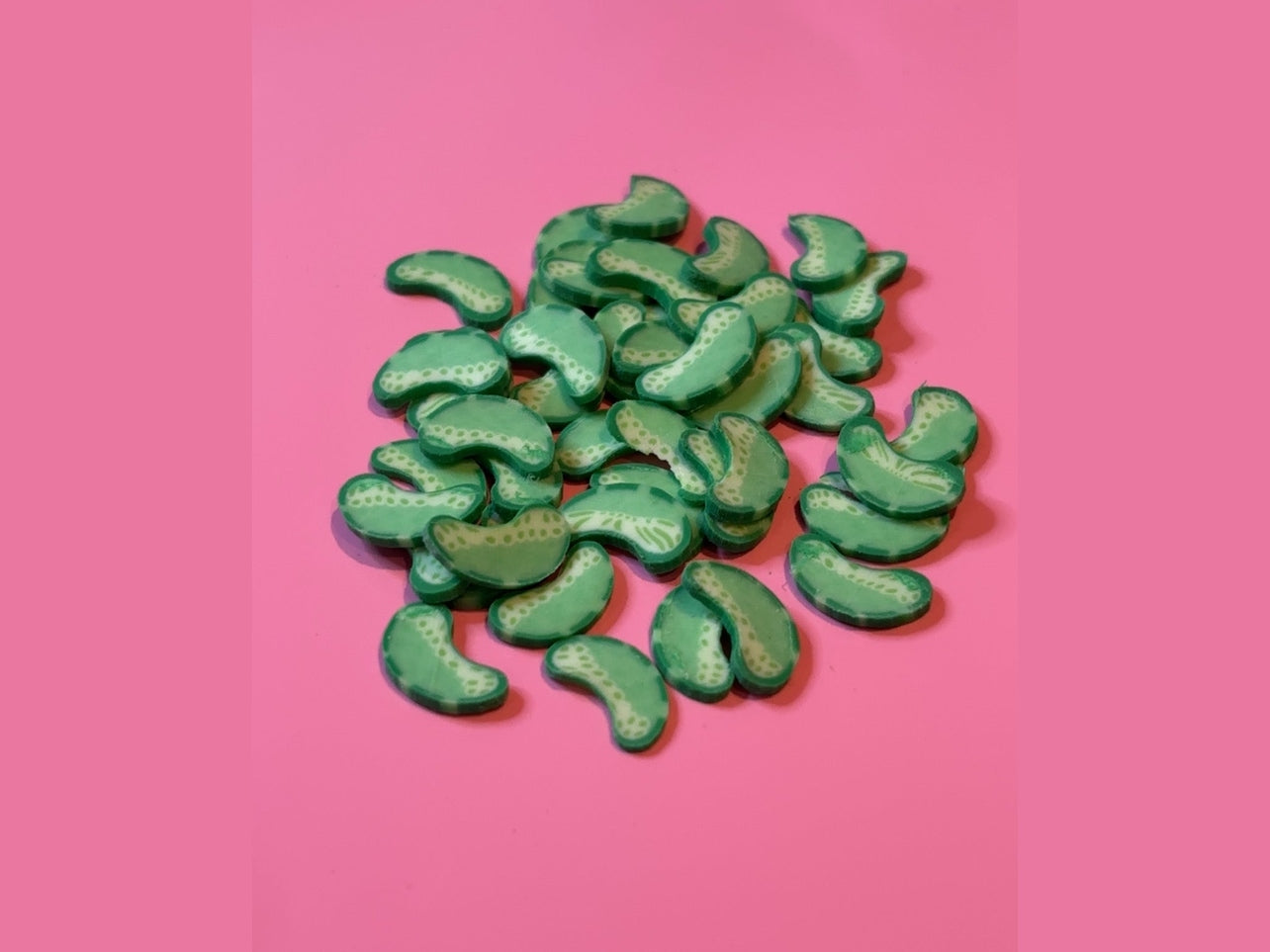 Green crescent-shaped Little Pickles with white dotted texture on pink background