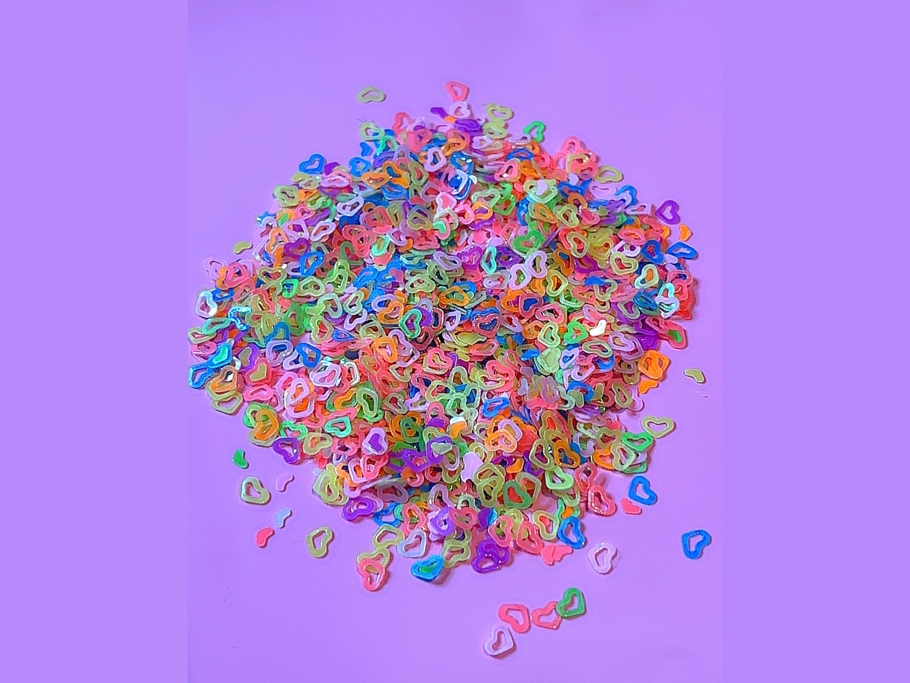 Multicolored hollow heart-shaped glitter pieces on purple background