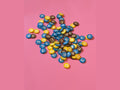 M&M's candy shaped resin charms in blue yellow and brown with white m logo on pink background