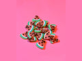 Watermelon clay slices with pink flesh, black seeds, and green rind on pink background