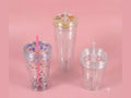 Three 16oz double lid tumblers with star confetti, gold and clear lids, and straws on pink background