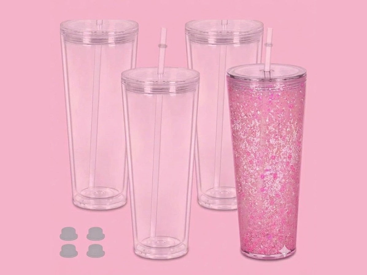Four 24oz clear double-walled tumblers with white straws and pink glitter liquid on pink background